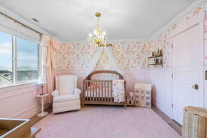 Bedroom with crown molding, an inviting chandelier, multiple windows, and a decorative wall