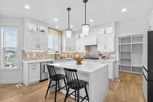 Kitchen with a kitchen breakfast bar, white cabinetry, a sink, appliances with stainless steel finishes, and light, waterfall style countertops