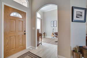Entryway with arched walkways, crown molding, light wood-type flooring, and baseboards