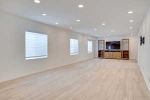 Unfurnished living room with recessed lighting, light wood-type flooring, and baseboards