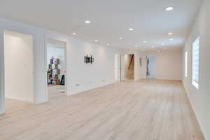 Unfurnished living room with stairs, light wood-style floors, recessed lighting, and baseboards