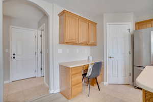 Office space featuring built in desk, light tile patterned floors, arched walkways, and baseboards
