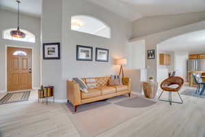 Living room with arched walkways, high vaulted ceiling, light wood-style floors, and baseboards