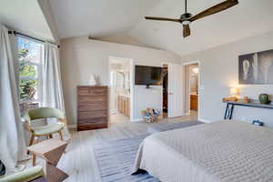 Bedroom featuring lofted ceiling, light wood-style floors, a walk in closet, ensuite bathroom, and baseboards