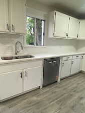 Kitchen with white cabinetry, a sink, light countertops, dishwashing machine, and backsplash