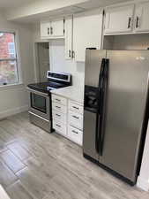 Kitchen featuring white cabinets, stainless steel appliances, light countertops, baseboards, and wood finish floors