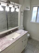 Full bathroom with walk in shower, vanity, toilet, and baseboards