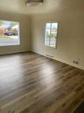 Empty room with dark wood-type flooring, visible vents, and a healthy amount of sunlight
