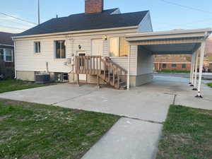 Rear view of property featuring concrete driveway, an attached carport, a chimney, a shingled roof, and central AC unit