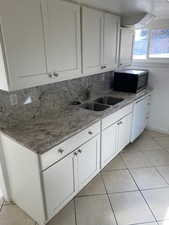 Kitchen with light tile patterned floors, stainless steel microwave, white cabinets, a sink, and dishwasher
