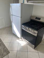 Kitchen with stainless steel gas range, light tile patterned flooring, light stone counters, and under cabinet range hood