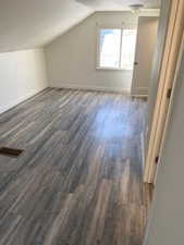 Additional living space with a textured ceiling, visible vents, dark wood-style floors, baseboards, and vaulted ceiling