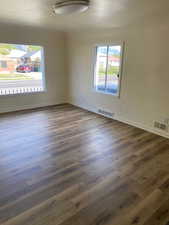Unfurnished room featuring visible vents, dark wood-style flooring, and baseboards