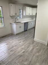 Kitchen featuring white cabinets, stainless steel dishwasher, light wood-style flooring, and baseboards