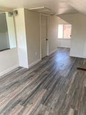 Spare room with a textured ceiling, baseboards, vaulted ceiling, and dark wood-type flooring