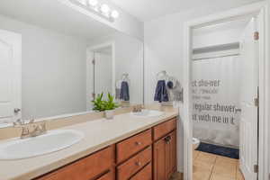 Full bathroom with toilet, double vanity, a sink, and tile patterned floors