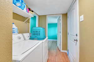 Laundry room featuring a textured ceiling, a textured wall, baseboards, washer and clothes dryer, and light wood finished floors