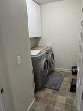 Washroom with baseboards, stone finish flooring, washer and dryer, and cabinet space
