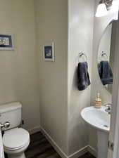 Half bathroom with baseboards, wood finished floors, toilet, and a sink