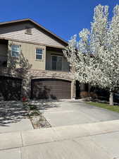 View of front of home featuring driveway, a balcony, stone siding, an attached garage, and stucco siding