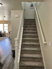 Stairs featuring a textured ceiling, wood finished floors, and baseboards