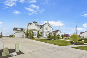 View of front facade featuring a chimney, stone siding, a front lawn, concrete driveway, and an attached garage