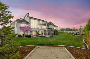 Back of house with a balcony, a patio area, a lawn, a chimney, and stucco siding