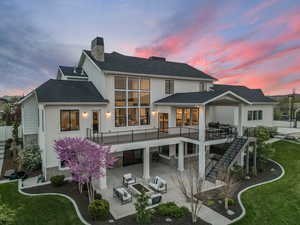 Back of property at dusk with a chimney, a patio area, outdoor lounge area, a shingled roof, and stairway