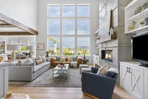 Living area featuring a chandelier, beam ceiling, a glass covered fireplace, light wood finished floors, and a high ceiling