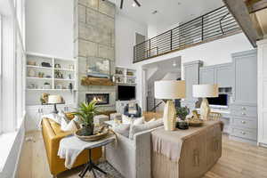 Living area featuring a fireplace, light wood-style floors, a ceiling fan, and a high ceiling