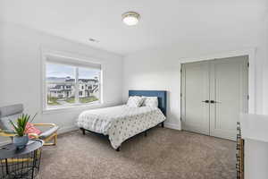 Carpeted bedroom with baseboards, visible vents, and a closet