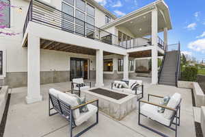 View of patio with an outdoor living space with a fire pit, stairs, and a balcony