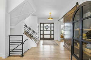 Entrance foyer featuring light wood finished floors, stairway, a barn door, baseboards, and french doors
