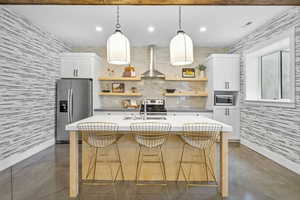Kitchen with stainless steel appliances, open shelves, wall chimney range hood, a sink, and concrete flooring