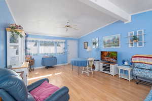 Living area featuring ceiling fan, wood finished floors, lofted ceiling with beams, and ornamental molding