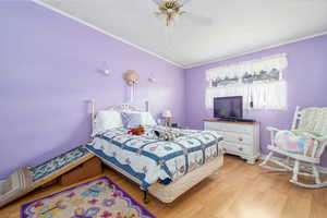 Bedroom with baseboards, light wood-type flooring, ceiling fan, and crown molding