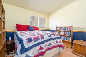 Bedroom with lofted ceiling, wainscoting, and wood finished floors