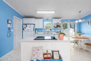 Kitchen featuring freestanding refrigerator, light countertops, black electric cooktop, a sink, and crown molding