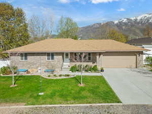 Ranch-style home featuring roof with shingles, concrete driveway, an attached garage, brick siding, and a front yard