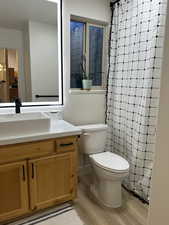 Full bathroom with toilet, vanity, curtained shower, and wood finished floors