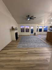 Living area featuring a fireplace with flush hearth, baseboards, a textured ceiling, wood finished floors, and ceiling fan with notable chandelier