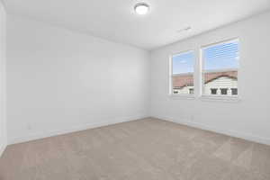 Empty room with light colored carpet, visible vents, and baseboards