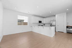 Kitchen with stainless steel appliances, a kitchen bar, light wood-type flooring, a peninsula, and light countertops