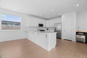 Kitchen with light wood-style flooring, a breakfast bar area, appliances with stainless steel finishes, light countertops, and a peninsula