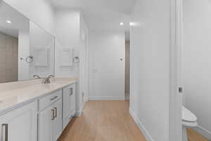 Full bath featuring double vanity, wood finished floors, baseboards, and a sink