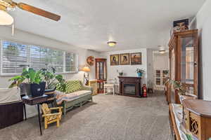 Living area featuring a textured ceiling, ceiling fan, carpet floors, and a fireplace