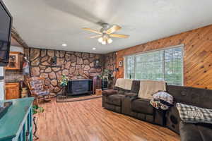 Living area with a wood stove, ceiling fan, wooden walls, a textured ceiling, and wood finished floors