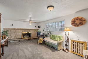 Carpeted living room featuring a ceiling fan, a textured ceiling, and a fireplace