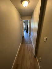 Hall featuring a textured ceiling, wood finished floors, and baseboards