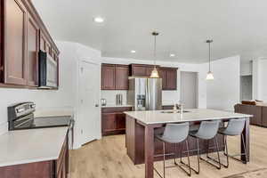 Kitchen featuring light wood-style floors, a kitchen bar, appliances with stainless steel finishes, light countertops, and a sink
